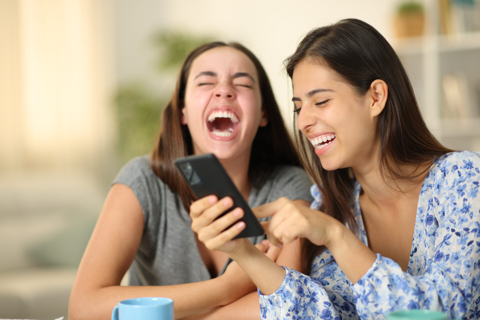 Two happy friends laughing hilarious using phone together at home