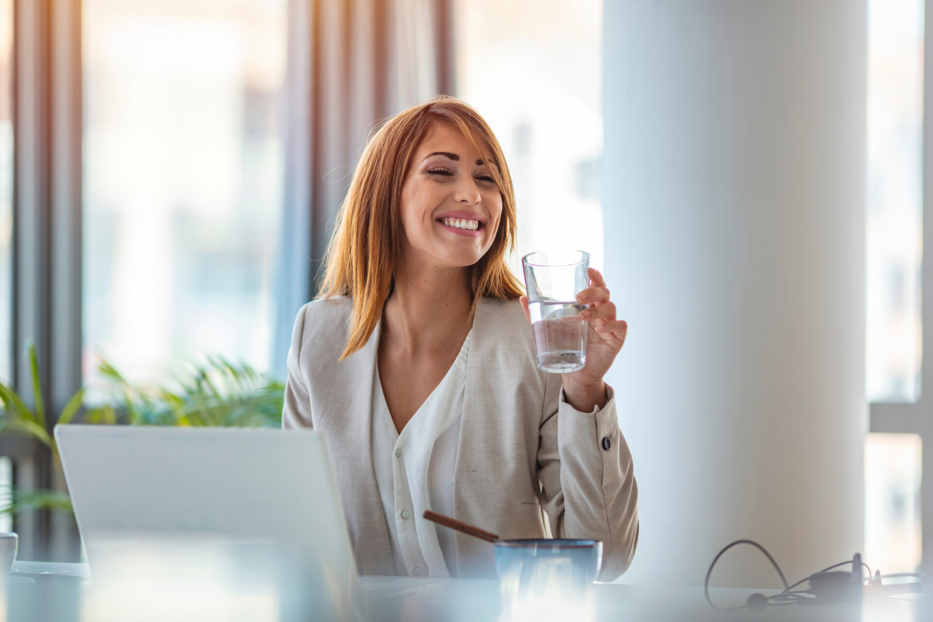 Businesswoman drinking water while working in her office. Close up of woman using a computer while holding a glass of water. Dehydrated female office worker drinking still mineral water